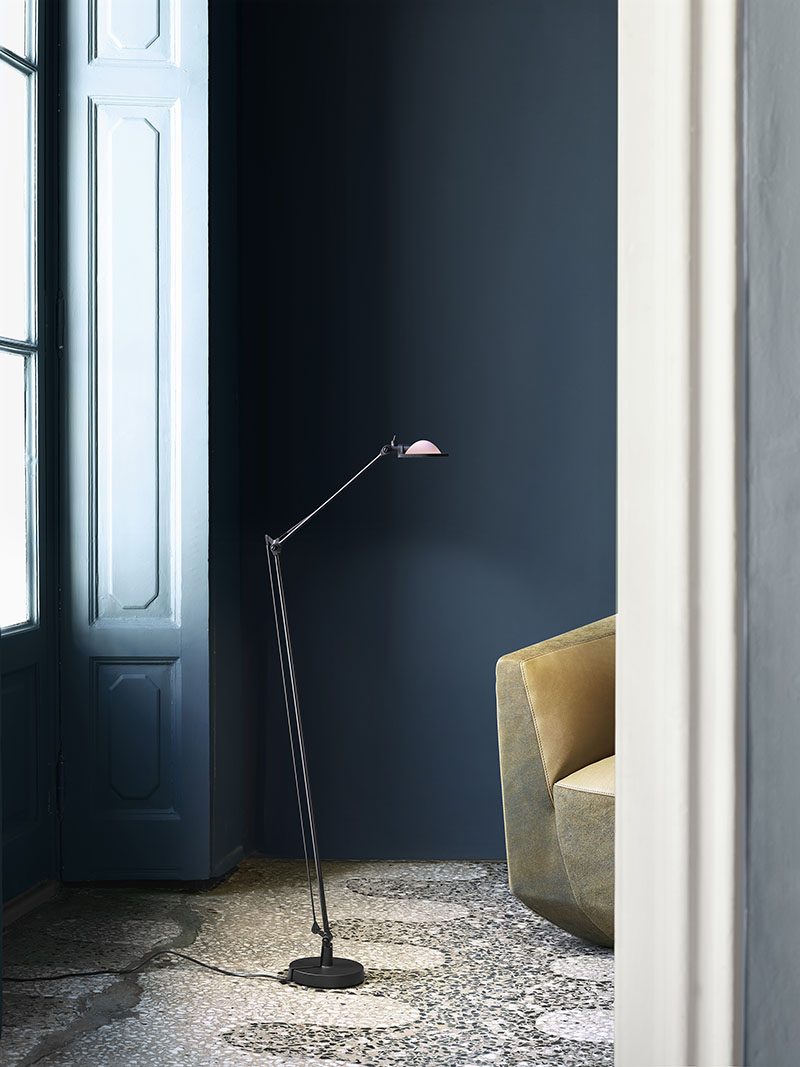 Luceplan: en una habitación de paredes en gris elegante con un ventanal por el que entra la luz natural hay una lámpara de pie Luceplan sobre una alfombra estampada y junto a un sofá en color arena.