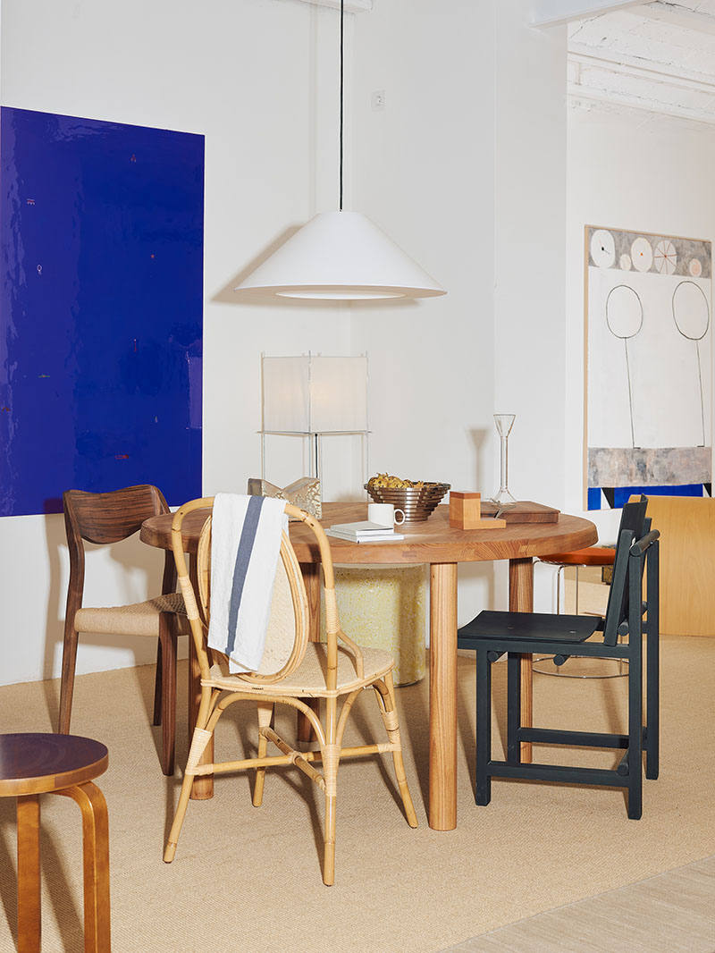 Zona de comedor de Matèria, tienda de mobiliario en Barcelona, con una mesa redonda de madera y lámpara colgante