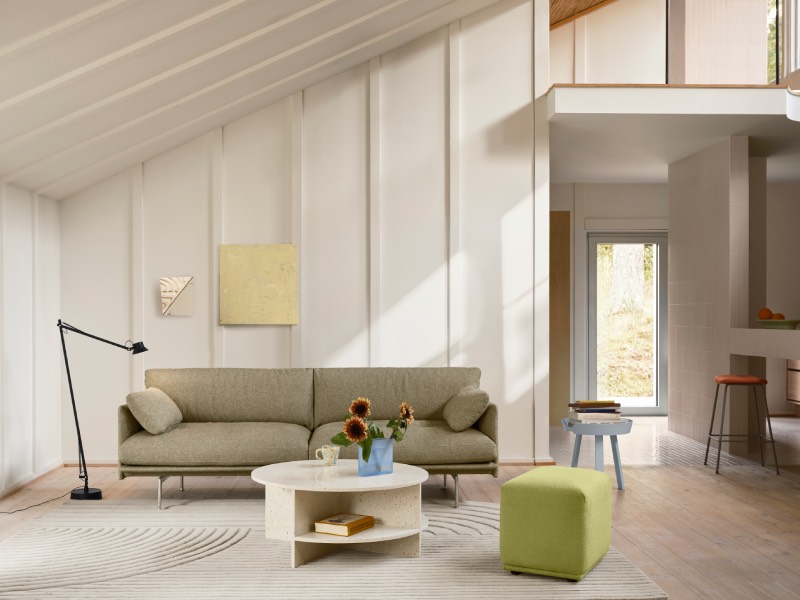 Muuto Halves MSDS Studio: salón abuhardillado en tonos claros con ventanales que dejan pasar la luz natural, una lámpara de pie negra, un sofá en color tierra, una mesa de centro redonda y un cubo en color verde pistacho para sentarse.