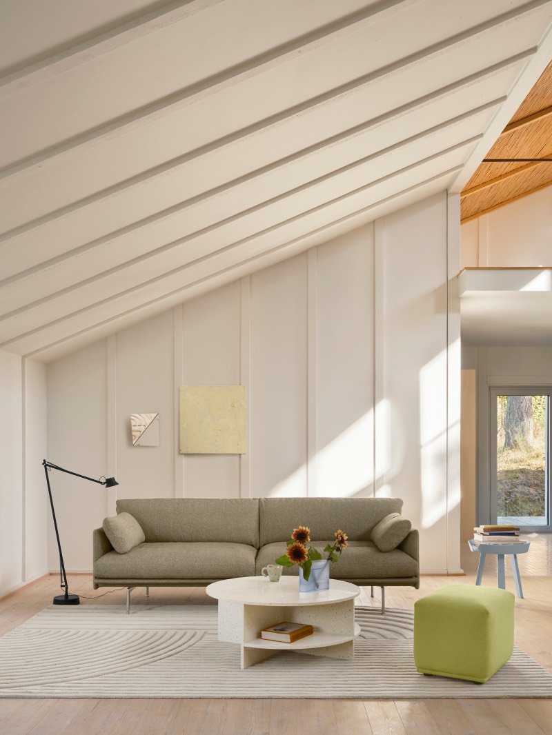 Muuto Halves MSDS Studio: salón abuhardillado en tonos claros con ventanales que dejan pasar la luz natural, una lámpara de pie negra, un sofá en color tierra, una mesa de centro redonda y un cubo en color verde pistacho para sentarse.