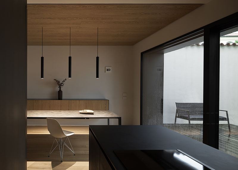 QB Atelier organiza en PDS House la cocina con mobiliario oscuro y salida directa a un pequeño patio