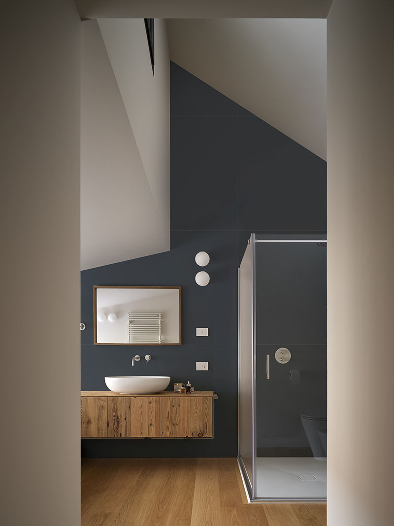 QB Atelier resuelve en PDS House un baño con revestimientos oscuros, carpintería de madera y ducha acristalada