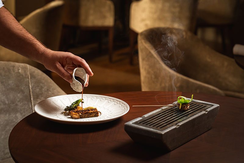 Servicio en mesa del Restaurante Suba en Lisboa con salsa vertida sobre el plato y bocado ahumado aparte