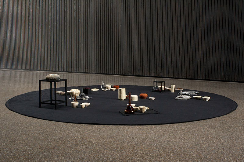 Sara García vincula la hospitalidad a un montaje circular de piezas cerámicas y objetos dispuestos sobre un gran tapiz negro