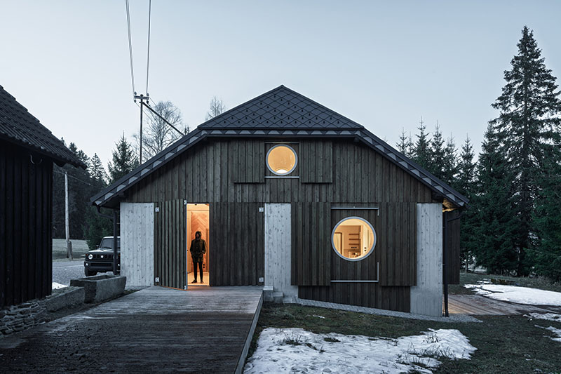 Studio Plyš muestra la fachada principal de Casa Borová Lada con puertas correderas y ventanas circulares iluminadas