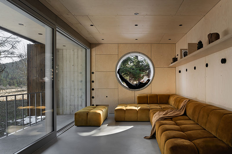Studio Plyš abre el estar de Casa Borová Lada con un ventanal circular y un sofá modular en tono mostaza
