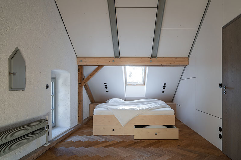 Studio Plyš organiza el dormitorio principal de Casa Borová Lada bajo cubierta con cama de madera y lucernario