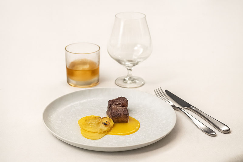 Plato de carne acompañado por un vaso de whisky, perteneciente a la experiencia The Blue Odyssey de Johnie Walker Blue