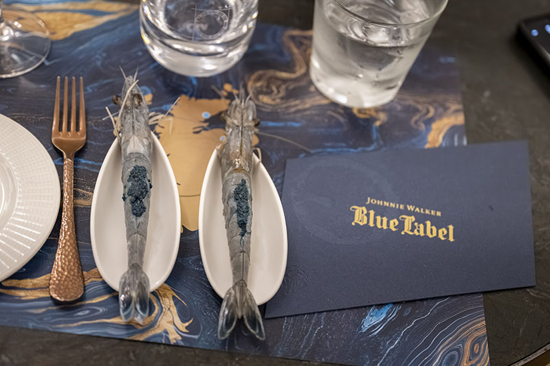 Plato de gambas junto a una tarjeta corporativa en The Blue Odyssey de Johnie Walker Blue
