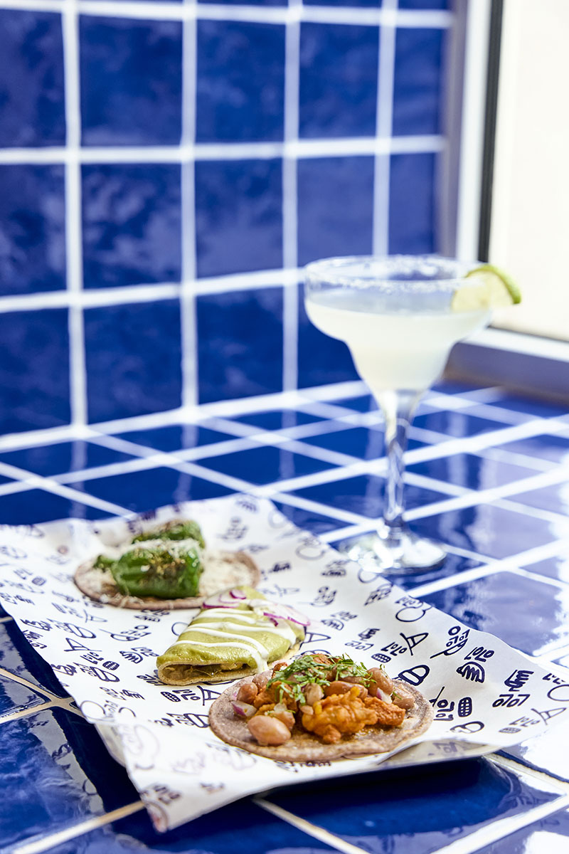 Lolo Taco Bar y Carne muestran un cóctel junto a tacos sobre azulejo azul