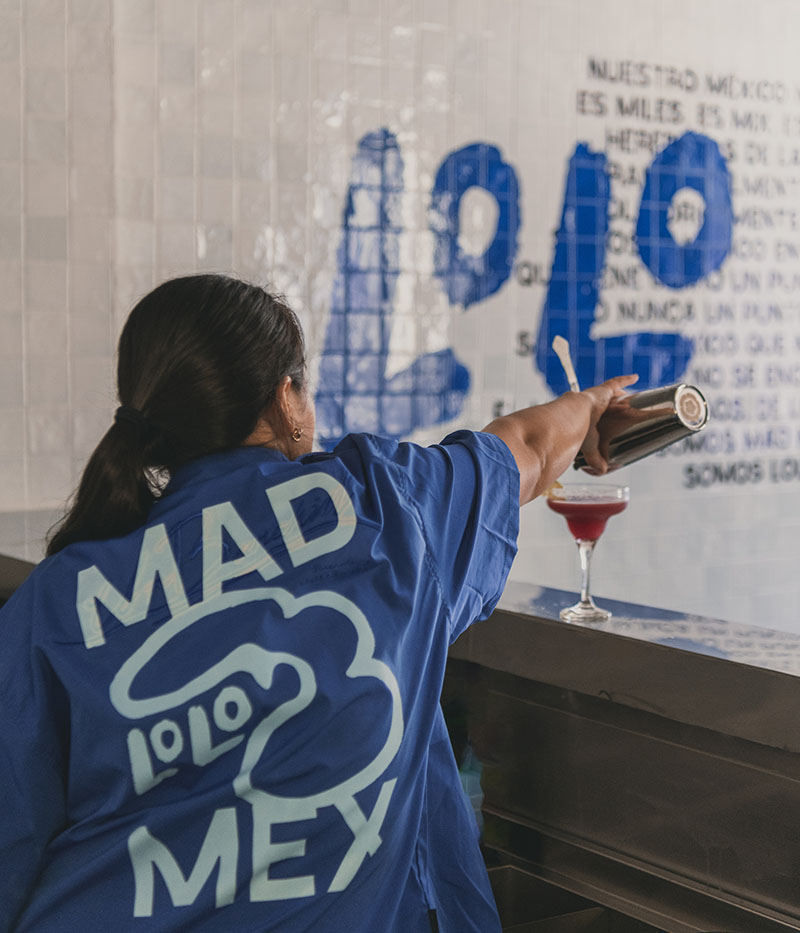 Lolo Taco Bar y Carne muestran a una trabajadora que sirve un cóctel frente al muro con la gráfica del proyecto