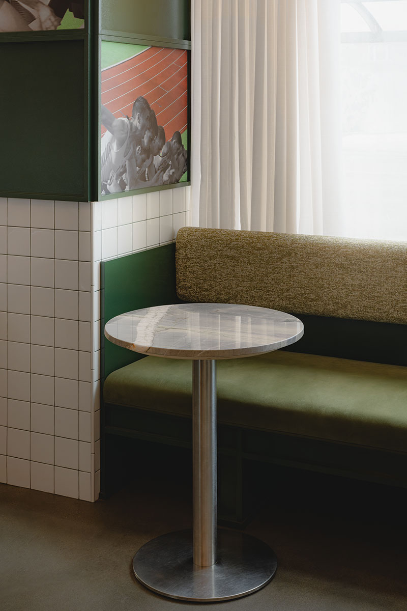 Ste Marie sitúa en Va! una mesa de mármol junto a un banco verde y paneles ilustrados